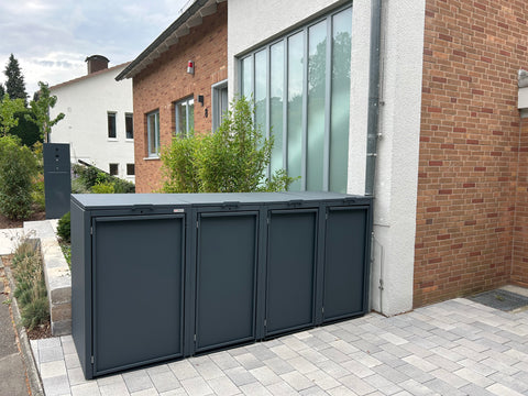 BIO Stefan Mülltonnenbox 4er in anthrazit vor einem Ziegelhaus.