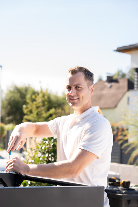 Ein Mann montiert eine BIO Stefan Mülltonnenbox im Garten.