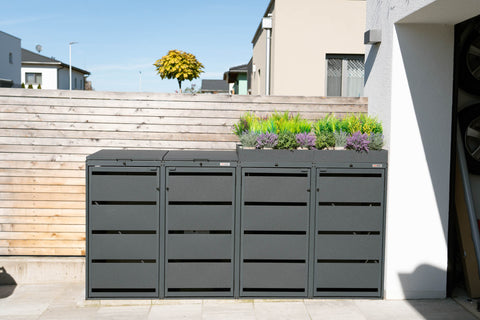 Mülltonnenbox von BIO Stefan mit Pflanzdach vor einem Holzzaun.