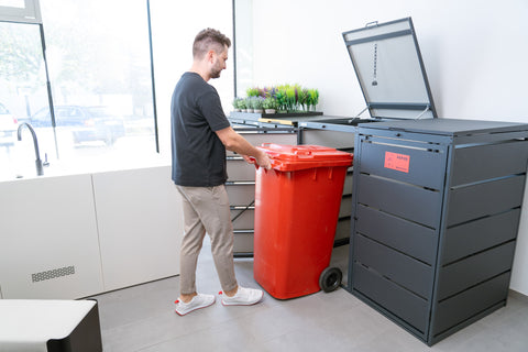 Mann stellt einen roten Müllcontainer in eine BIO Stefan Mülltonnenbox.