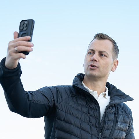 Eine Person in schwarzer Jacke hält ein Smartphone in die Luft.