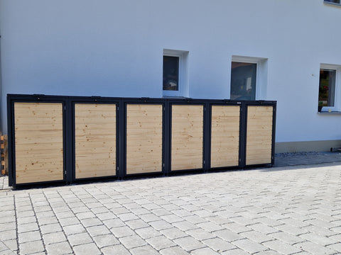 Kundenfoto einer BIO Stefan Mülltonnenbox aus Holz und Metall mit sechs Fächern vor einer weißen Hauswand