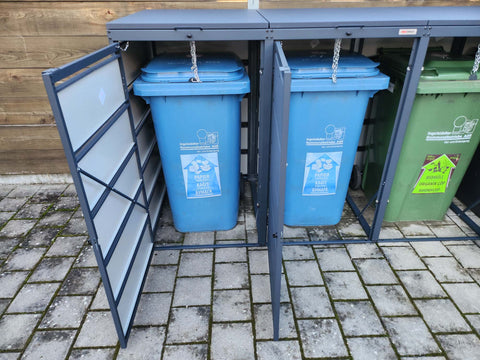 Kundenfoto: Anthrazitfarbene BIO Stefan Mülltonnenbox mit geöffneten Türen, dahinter zwei blaue Papiertonnen und eine grüne Tonne auf Pflaster
