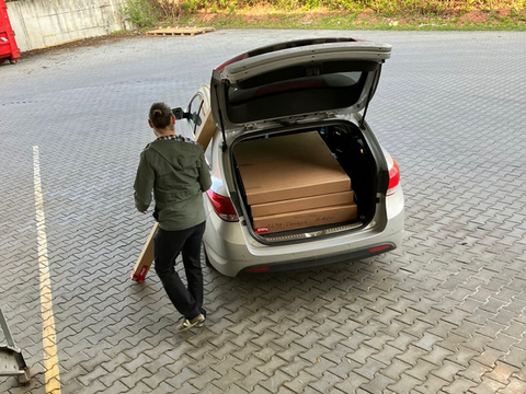 BIO StefanPersoon laadt dozen met producten in de kofferbak van een grijze auto.