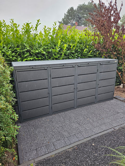 Gray 4-bin garbage can box from BIO Stefan on paved ground in front of a green hedge.