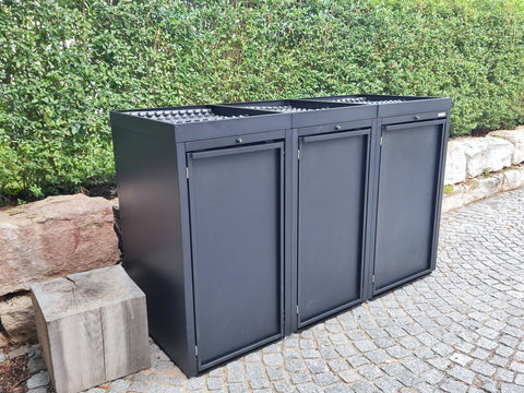 Schwarze 3er-Mülltonnenbox von BIO Stefan vor Gartenhecke.