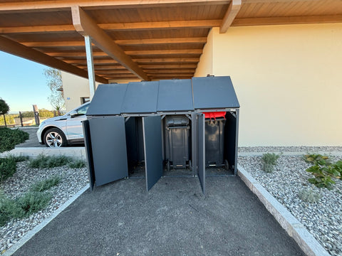 Mülltonnenbox von BIO Stefan für vier Tonnen geöffnet vor Garage.