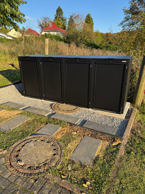 Schwarze BIO Stefan Mülltonnenbox für vier Tonnen im Freien auf Steinboden.