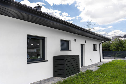 Moderne schwarze Mülltonnenbox neben einem weißen Gebäude vor blauem Himmel.