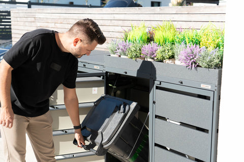Mann öffnet Bio Stefan Mülltonnenbox mit Pflanzdach und entleert Mülltonne.