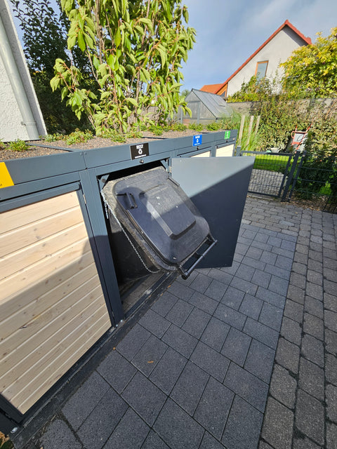 Mülltonnenbox aus Holz von Bio Stefan mit offener Restmülltonne vor einem Garten.