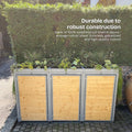 Waste garbage can box made of weatherproof steel, decorated with plants, in front of a green hedge.