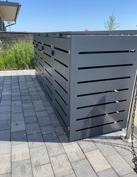 BIO Stefan Alubert Mülltonnenbox 4er in Anthrazit steht auf gepflasterter Terrasse neben hohem Gras
