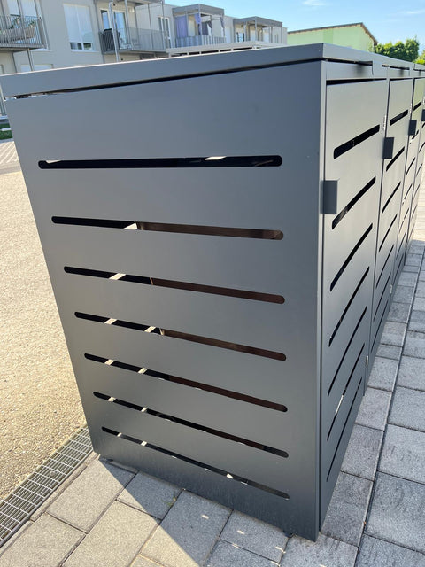 BIO Stefan Mülltonnenbox Alubert 4er anthrazit steht seitlich auf Pflaster vor Mehrfamilienhaus