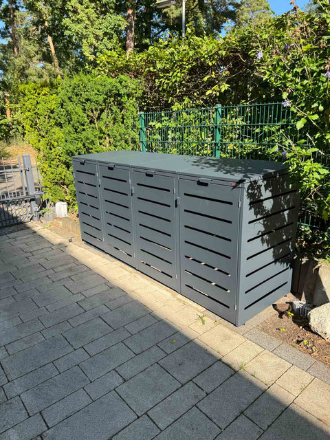 BIO Stefan Alubert Mülltonnenbox 4er 240l in Anthrazit steht auf gepflasterter Einfahrt vor grüner Garteneinfassung