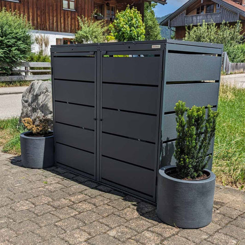 BIO Stefan Mülltonnenbox Dagobert 2er 240l in Anthrazit, freistehend vor Haus mit zwei Pflanzkübeln