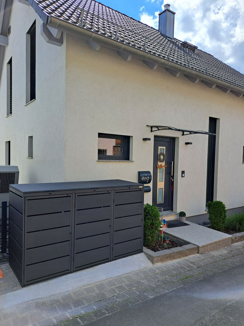 BIO Stefan Dagobert Mülltonnenbox 3er 240l in Anthrazit mit Deckel neben dem Hauseingang eines hellen Einfamilienhauses