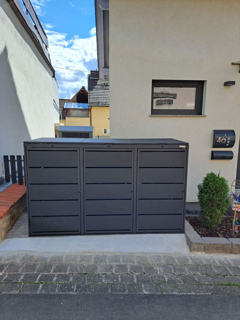 BIO Stefan Dagobert Mülltonnenbox 3er 240l in Anthrazit mit Deckel auf ebener Betonfläche vor der Fassade, daneben Beet mit Thuja