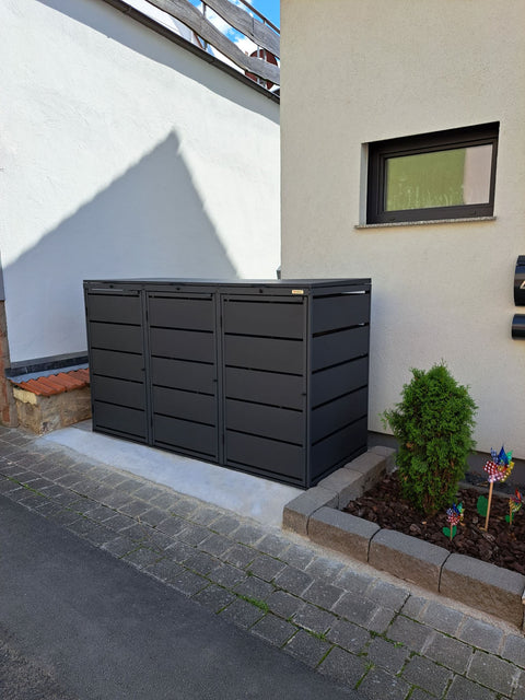 BIO Stefan Dagobert Mülltonnenbox 3er 240l in Anthrazit mit Deckel in Seitenansicht an der Hauswand neben dem eingefassten Beet