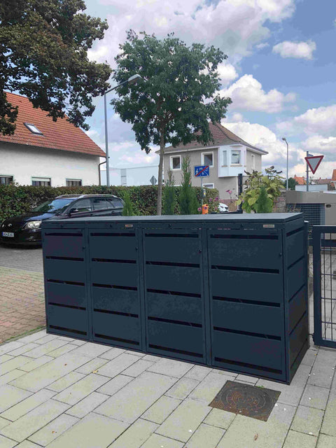BIO Stefan Dagobert Mülltonnenbox 4er 120l in Anthrazit steht auf gepflasterter Einfahrt vor Wohnhäusern