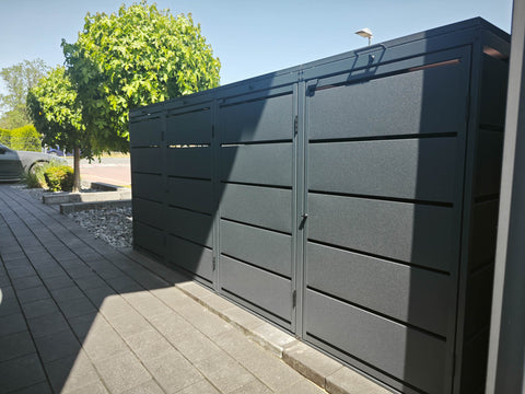 BIO Stefan Mülltonnenbox Dagobert 4er 240l in Anthrazit steht links neben gepflasterter Einfahrt vor Baum