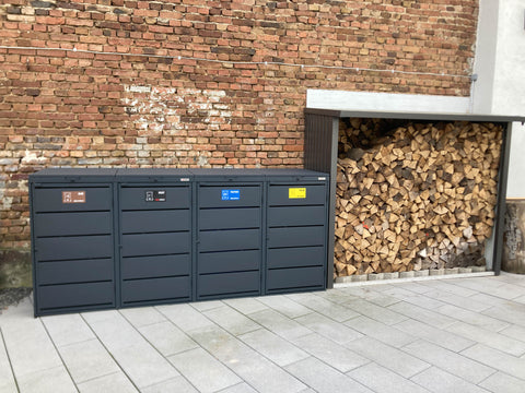 BIO Stefan Dagobert Mülltonnenbox 4er 240l in Anthrazit vor Backsteinwand neben Holzlager