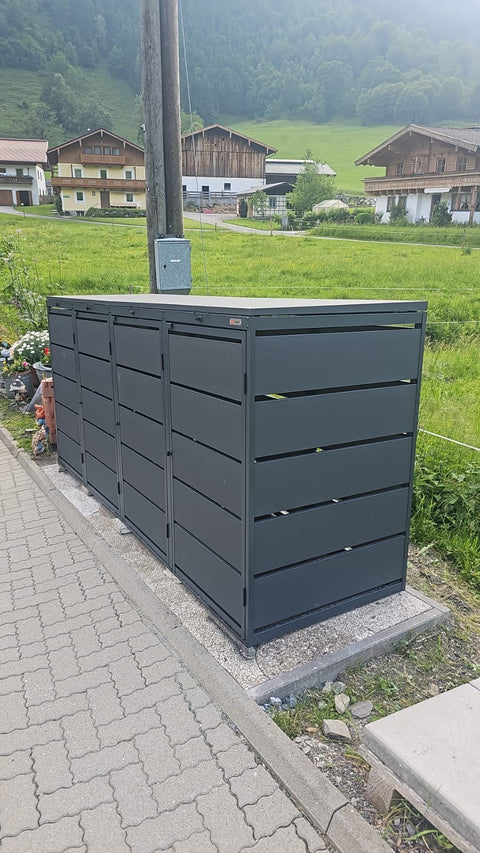 BIO Stefan Dagobert Mülltonnenbox 4er 240l in Anthrazit am Straßenrand vor Häusern in ländlicher Umgebung