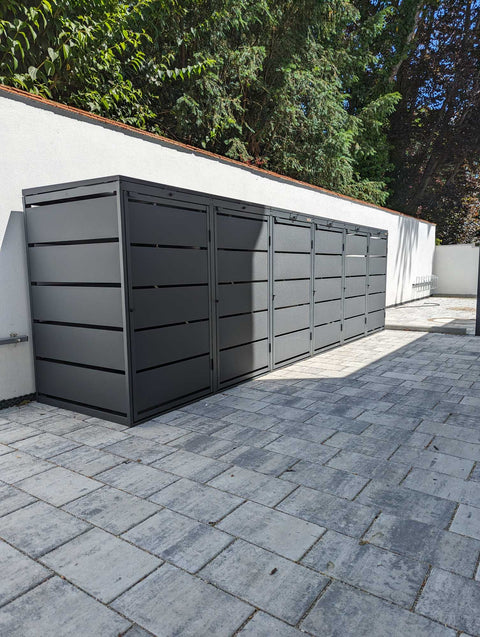 BIO Stefan Dagobert Mülltonnenbox 6er 240l in Anthrazit als durchgehende Reihe an der Hofmauer auf Pflaster, Seitenansicht mit Lamellen und Klappdeckel