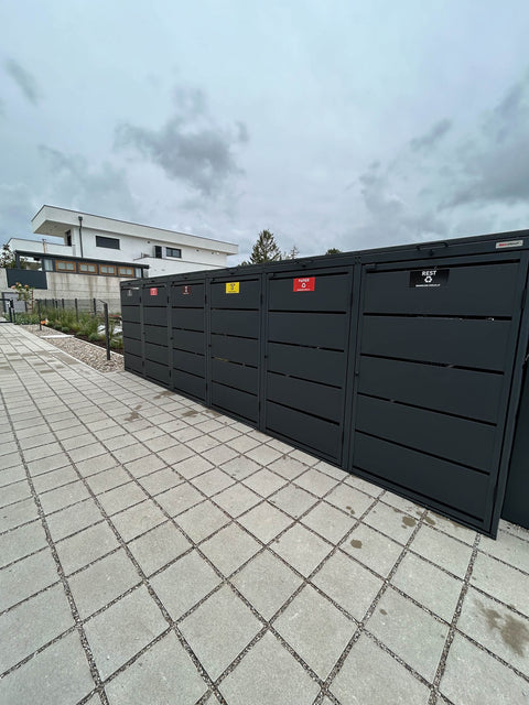 BIO Stefan Dagobert Mülltonnenbox 6er 240l in Anthrazit im Weitwinkel entlang der Reihe, Fach für Restmüll im Vordergrund, Lamellenfront mit Mülltrennungsschildern