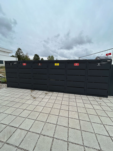 BIO Stefan Dagobert Mülltonnenbox 6er 240l in Anthrazit als geschlossene Reihe mit Klappdeckeln auf Betonplatten mit Splittfugen in einer Neubausiedlung
