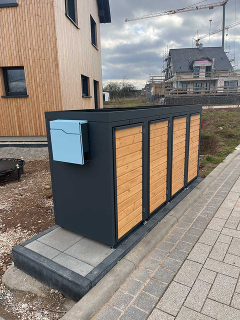BIO Stefan Holzmichl Mülltonnenbox 4er 120l anthrazit mit Holzfront und Paketbox vor Holzhaus im Neubaugebiet