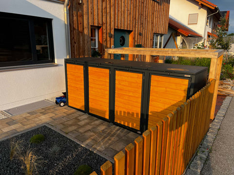 BIO Stefan Holzmichl Mülltonnenbox 4er 240l in Anthrazit mit Holzfront neben Hausfassade