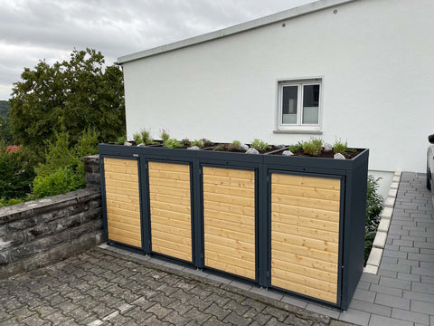 BIO Stefan Mülltonnenbox Holzmichl 4er 240l in Anthrazit mit Holzfront und bepflanztem Pflanzdach vor Haus