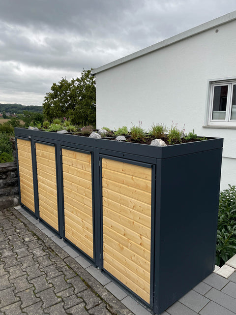 BIO Stefan Mülltonnenbox Holzmichl, 4er 240l anthrazit mit Holzfront und bepflanztem Pflanzdach vor Hauswand