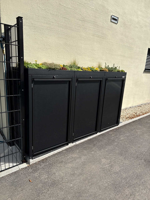 BIO Stefan Stahlfred Mülltonnenbox 3er 240l in Schwarz RAL 9005 mit Pflanzdach frontal an der Hauswand auf asphaltierter Zufahrt