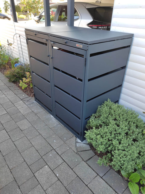 BIO Stefan Dagobert Muelltonnenbox 2er 120l in Anthrazit seitlich am Carport auf Pflasterweg neben Staudenbeet an weisser Holzfassade