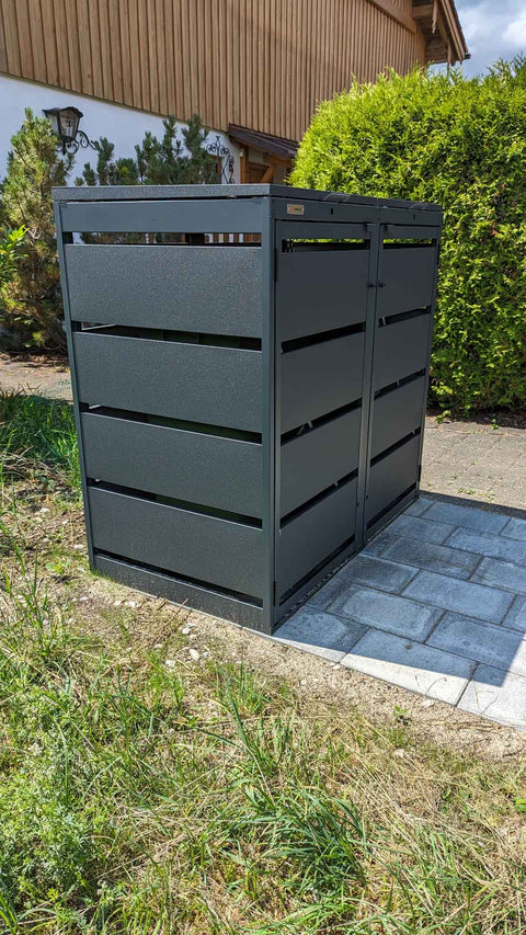 BIO Stefan Dagobert Muelltonnenbox 2er 120l in Anthrazit vor der Thujenhecke am Landhaus mit Holzfassade auf Pflasterflaeche
