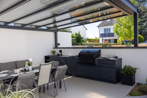Outdoor kitchen along the garden wall: long kitchen unit in anthracite beside the dining area