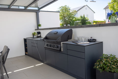 Outdoor kitchen along the garden wall: long kitchen unit in anthracite beside the dining area