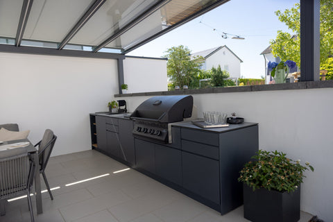 Outdoor kitchen along the garden wall: long kitchen unit in anthracite beside the dining area